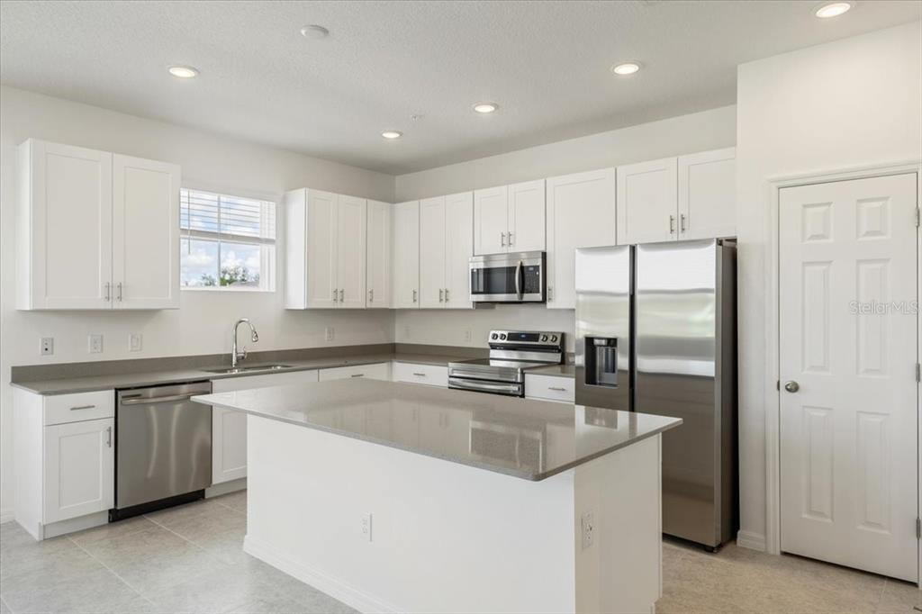 A modern kitchen features white cabinets, stainless steel appliances, and a central island with countertops — 1552 SILVER LINING WAY, APOPKA, FL