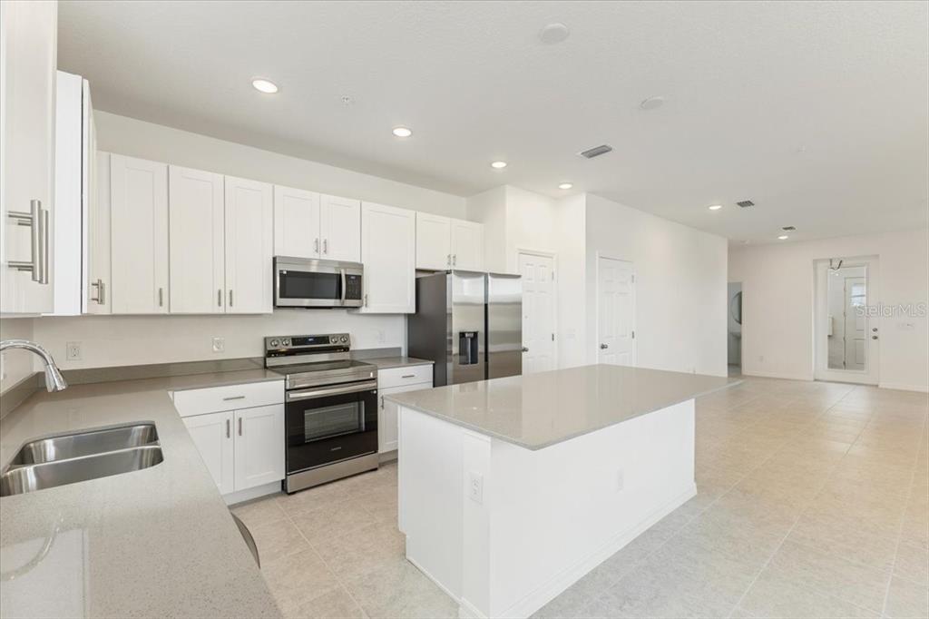 A modern kitchen features white cabinets, stainless steel appliances, and a large gray quartz island — 1552 SILVER LINING WAY, APOPKA, FL