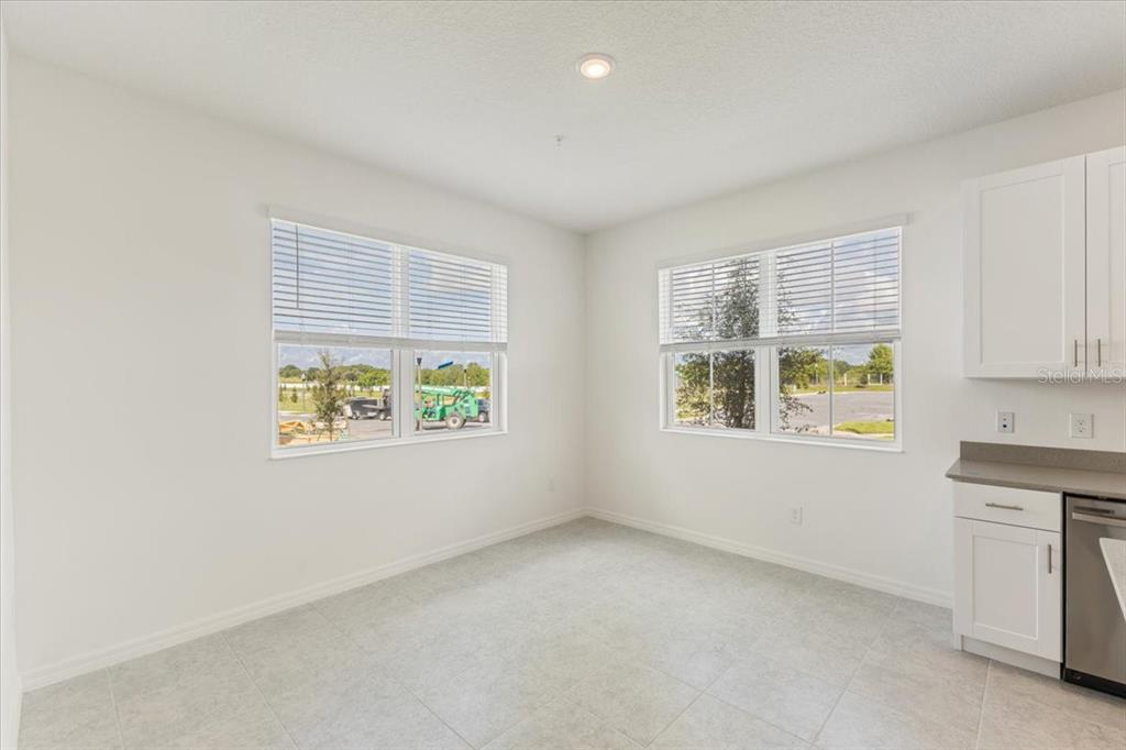 A bright, empty kitchen dining area features white walls, tile flooring, and two large windows — 1552 SILVER LINING WAY, APOPKA, FL