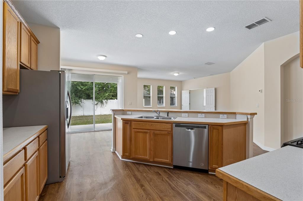 A kitchen with wood cabinets, stainless steel appliances, and a breakfast bar overlooking a living area — 4844 FLINT ROAD, WINDERMERE, FL