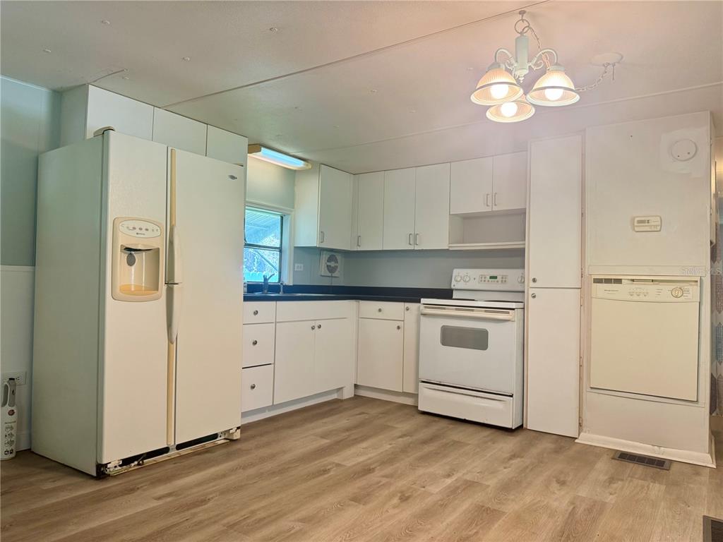 A kitchen with white cabinets, white appliances, dark countertops, and light wood-look flooring — 00 FREMONT LANE, SPRING HILL, FL