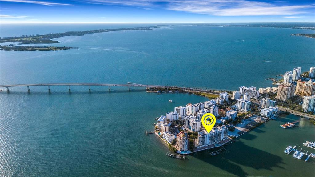 An aerial view shows a coastal condominium complex surrounded by water near a long bridge — 464 GOLDEN GATE POINT UNIT 403, SARASOTA, FL