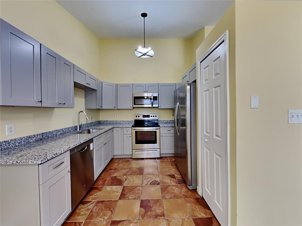 A kitchen features gray cabinets, granite countertops, stainless steel appliances, and brown tiled flooring — 502 SAN GABRIEL COURT, WINTER SPRINGS, FL