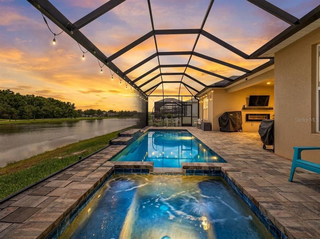 A screened-in patio features a swimming pool, a hot tub, and a lake view — 6946 TALAMORE DRIVE, WESLEY CHAPEL, FL