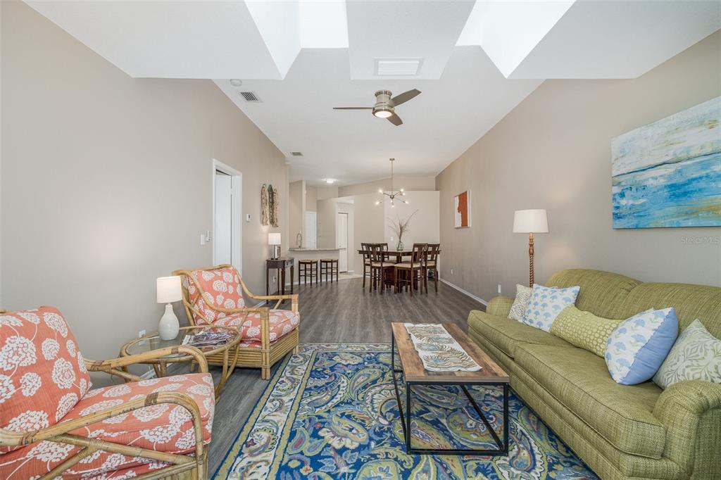 A dining area and living room with wood-look flooring, vaulted ceilings, and a sliding glass door — 3843 GOLDFINCH COURT, PALM HARBOR, FL