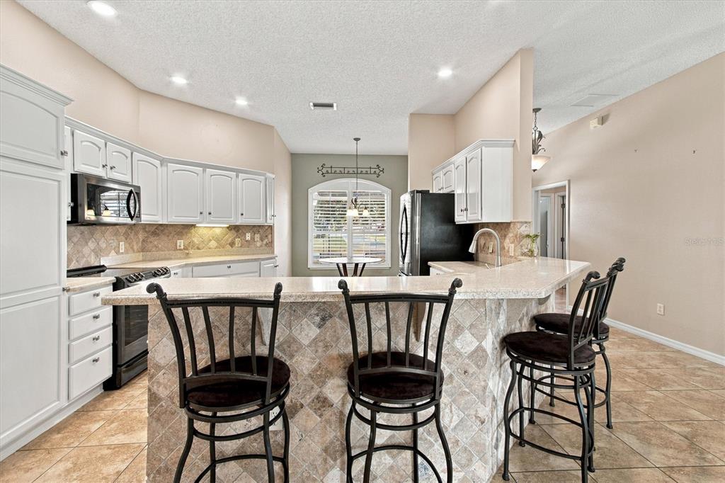 An open-concept dining area and kitchen with wood flooring, a breakfast bar, and white cabinetry — 2314 CALLAWAY DRIVE, THE VILLAGES, FL