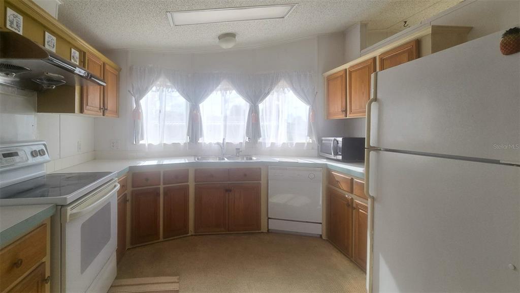 A kitchen features wood cabinets, white appliances, a double sink, and a window with curtains — 300 BEECH COURT, COCOA, FL