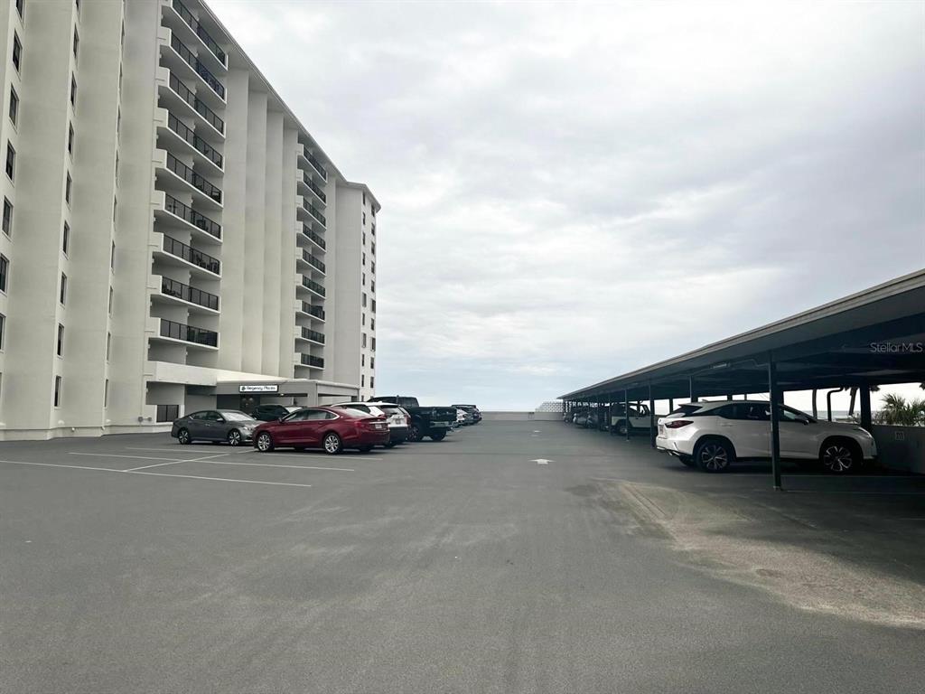 An outdoor parking lot features a tall apartment building and a covered parking structure — 1415 OCEAN SHORE BOULEVARD UNIT B060, ORMOND BEACH, FL