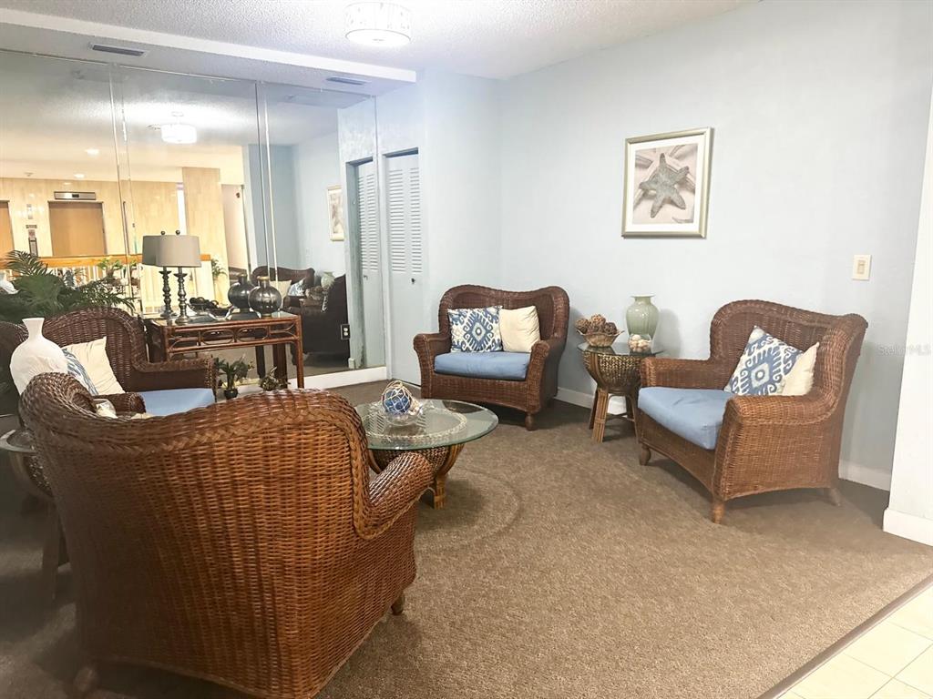 A living room features wicker chairs, a glass coffee table, and a large mirrored wall — 1415 OCEAN SHORE BOULEVARD UNIT B060, ORMOND BEACH, FL