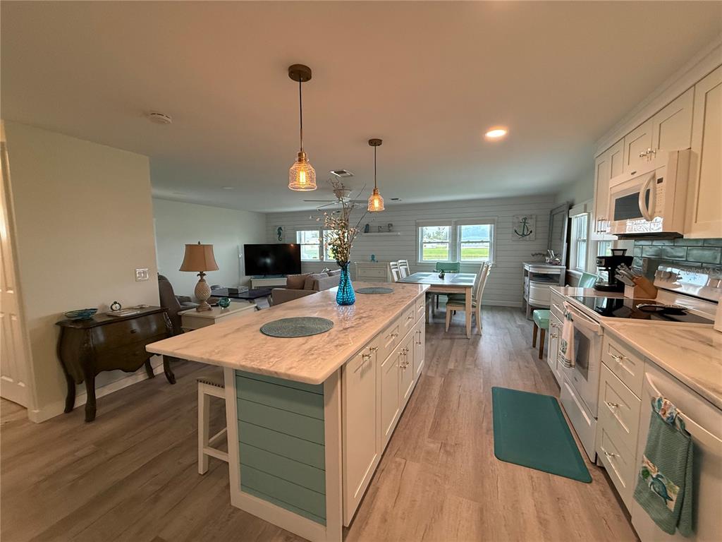 A kitchen with a large island, white cabinets, and light wood flooring opens to a living area — 637 LOS ALTOS UNIT 374, NORTH PORT, FL