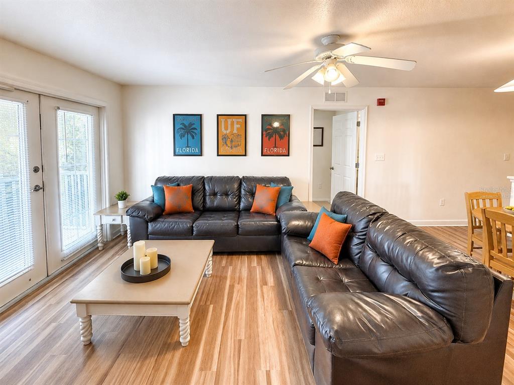 A living room features dark leather sofas, a coffee table, and three framed wall prints — 835 SW 9TH STREET UNIT 210, GAINESVILLE, FL