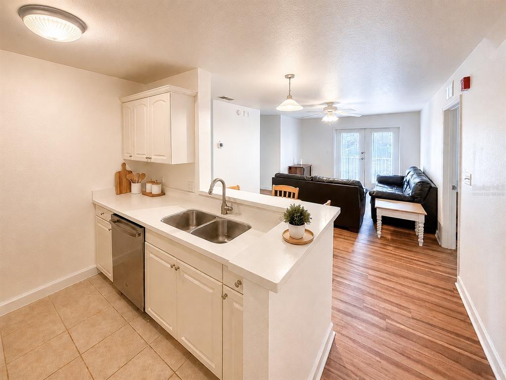 A kitchen with white cabinets and a double sink overlooks a living room with flooring — 835 SW 9TH STREET UNIT 210, GAINESVILLE, FL