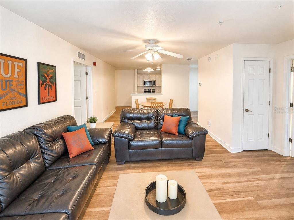A living room features dark leather sofas, wood-look flooring, and a view into the kitchen — 835 SW 9TH STREET UNIT 210, GAINESVILLE, FL