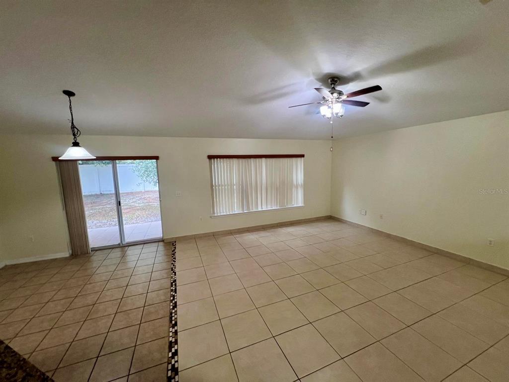 A spacious room with beige tile flooring, a ceiling fan, and a sliding glass door — 3401 HEATH DRIVE, DELTONA, FL