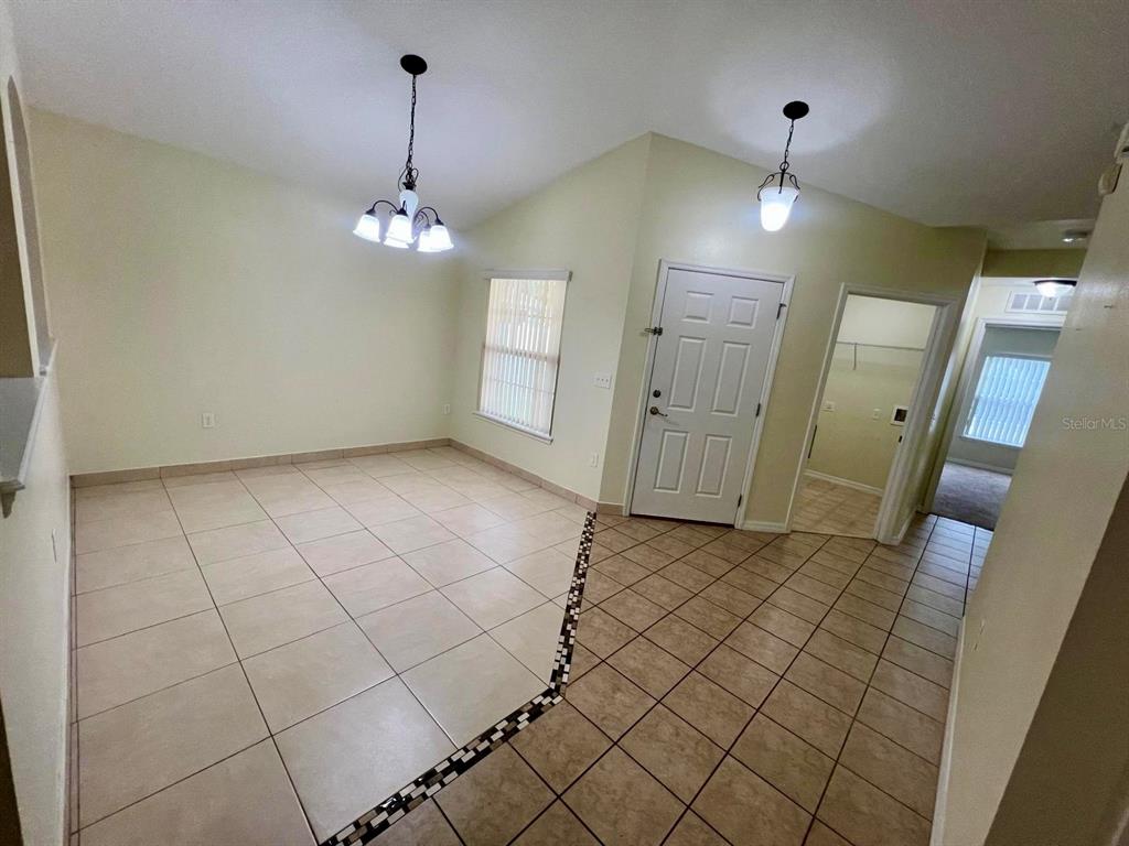 An empty dining area features light-colored tile flooring, a chandelier, and a white front door — 3401 HEATH DRIVE, DELTONA, FL
