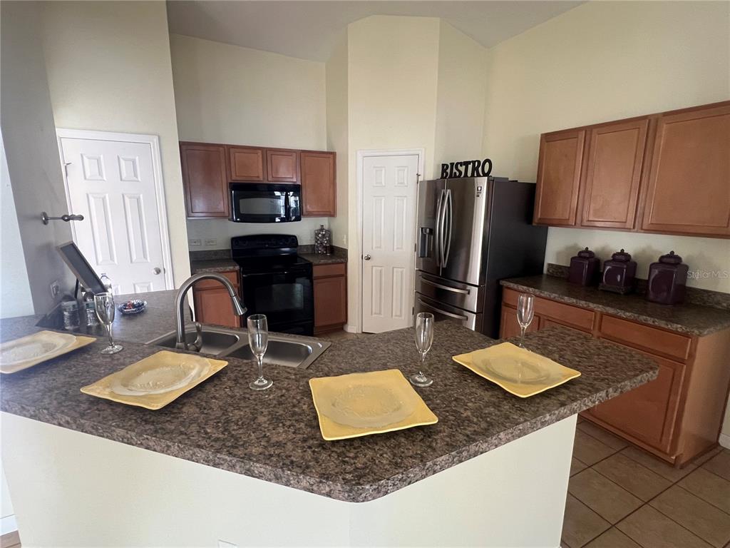 A kitchen features wood cabinets, dark countertops, stainless steel appliances, and a breakfast bar — 3401 HEATH DRIVE, DELTONA, FL