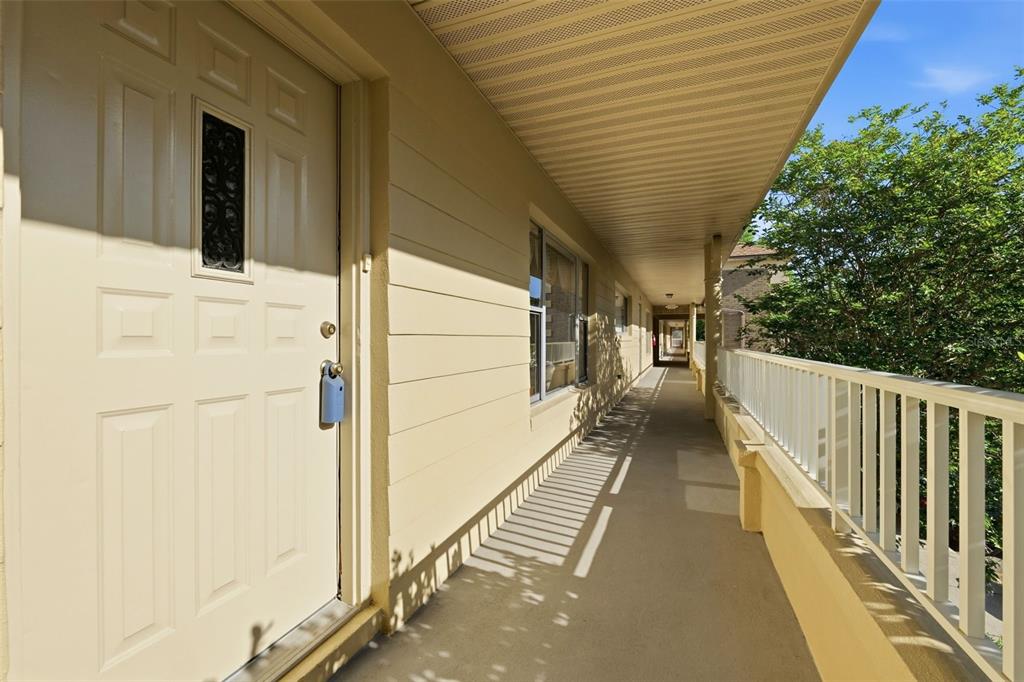 An exterior walkway with a cream-colored door, siding, and a white railing under a roof — 2192 SWEDISH DRIVE UNIT 26, CLEARWATER, FL