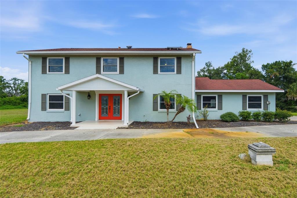 A two-story house with light blue stucco siding, a red front door, and a red roof — 7525 E APPLEWOOD DRIVE, INVERNESS, FL