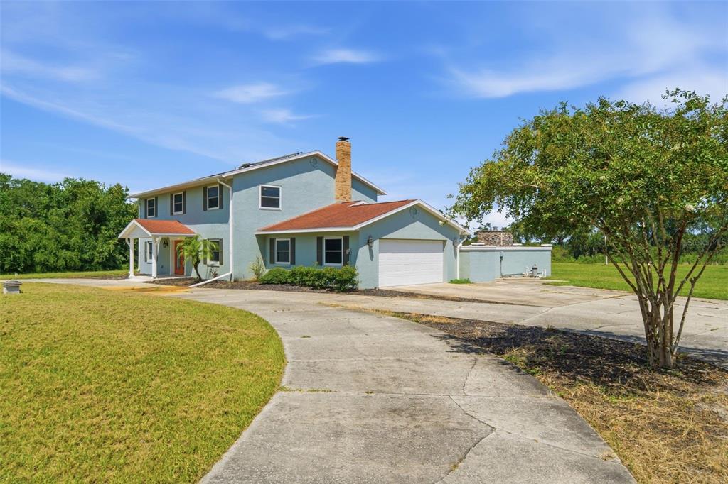 A two-story light blue house with a brick chimney and a concrete driveway — 7525 E APPLEWOOD DRIVE, INVERNESS, FL