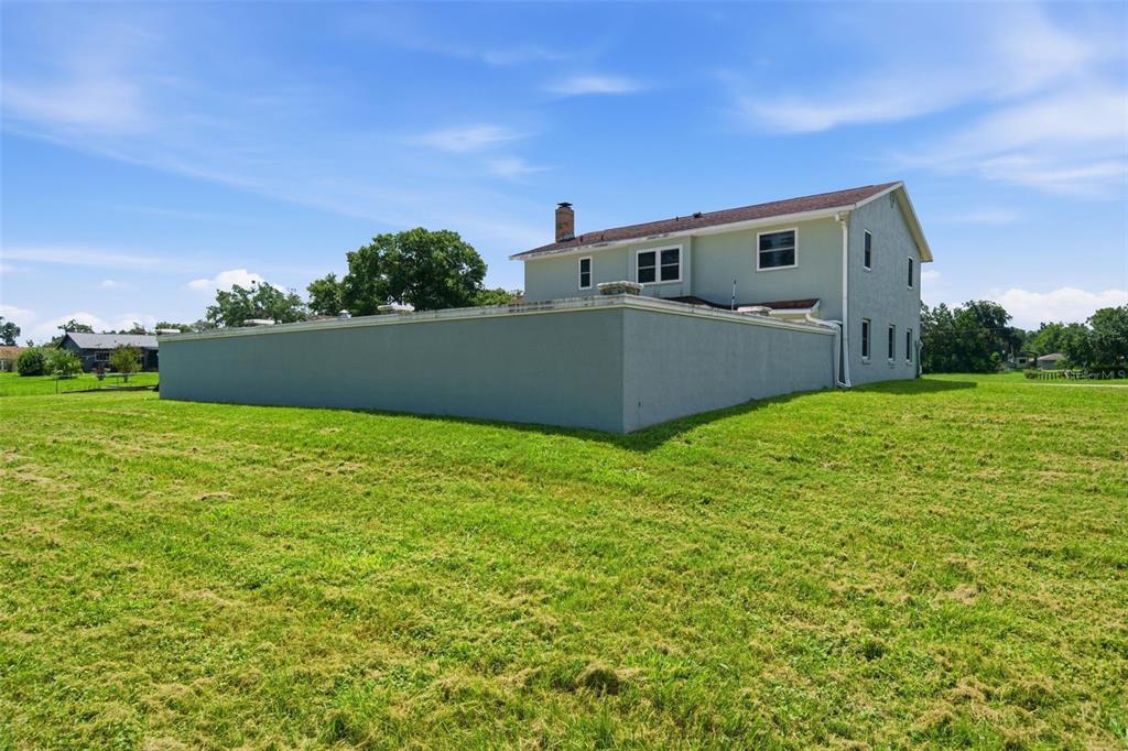 A two-story house with a large gray privacy wall stands on a grassy lot — 7525 E APPLEWOOD DRIVE, INVERNESS, FL