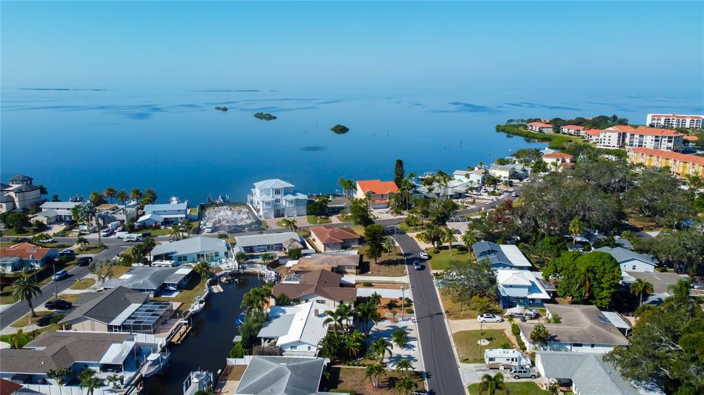 An aerial view shows a coastal neighborhood with houses, a canal, and the open water — 212 WESTWINDS DRIVE, PALM HARBOR, FL