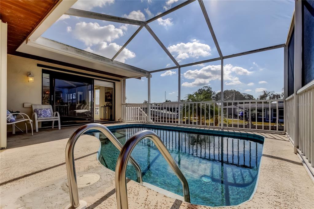 A screened-in patio features a small swimming pool with metal handrails and outdoor seating — 212 WESTWINDS DRIVE, PALM HARBOR, FL
