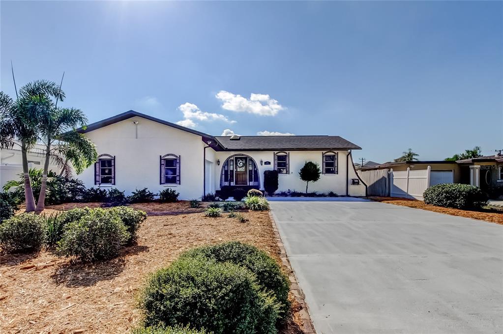 A white single-story house features a dark roof, arched entryway, and a concrete driveway — 212 WESTWINDS DRIVE, PALM HARBOR, FL