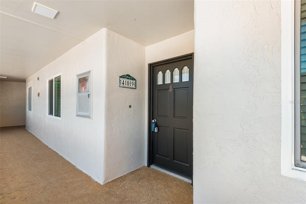 A dark front door with a lockbox sits on a covered walkway with white walls — 1776 6TH STREET NW UNIT 409, WINTER HAVEN, FL