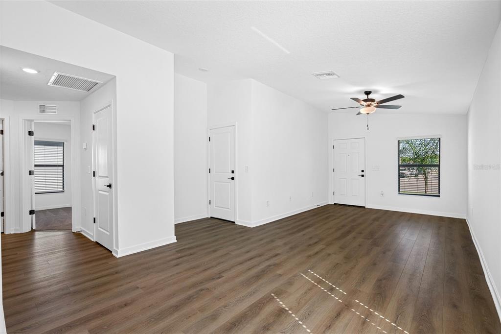 An empty room with white walls, wood-look flooring, a ceiling fan, and a front door — 11308 LINNET ROAD, WEEKI WACHEE, FL