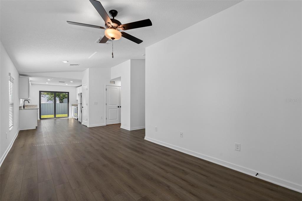 A spacious living area with wood-look flooring, a ceiling fan, and an adjacent kitchen — 11308 LINNET ROAD, WEEKI WACHEE, FL