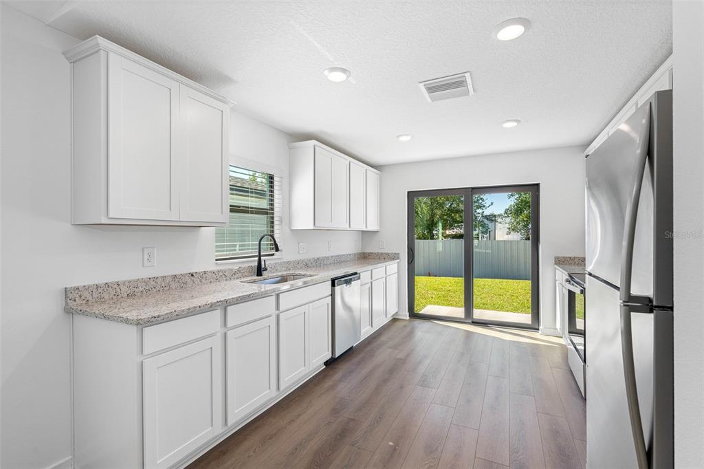 A bright kitchen features white cabinets, granite countertops, stainless steel appliances, and sliding glass doors — 11308 LINNET ROAD, WEEKI WACHEE, FL