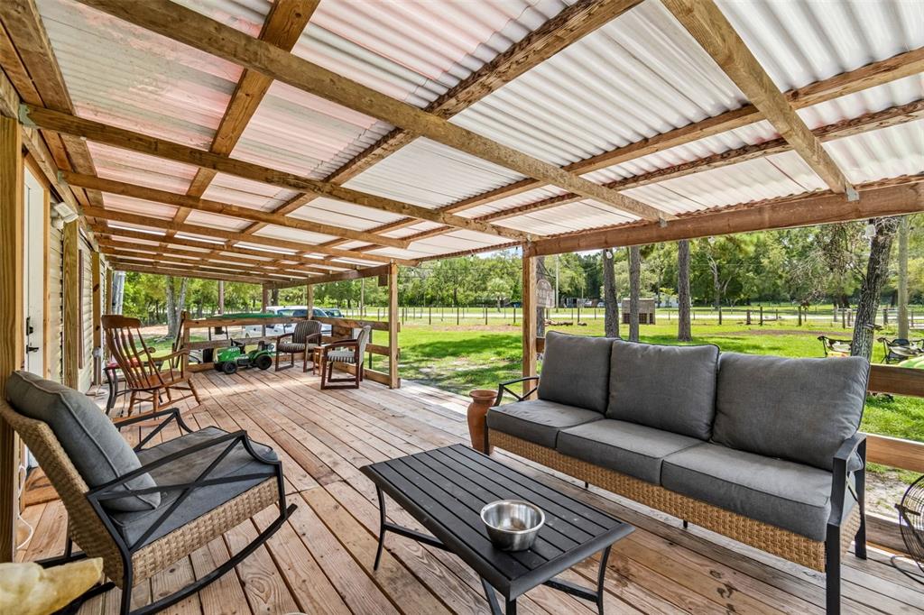 A covered wooden deck features outdoor seating, a coffee table, and a corrugated plastic roof — 18020 RIGSBY ROAD, SPRING HILL, FL