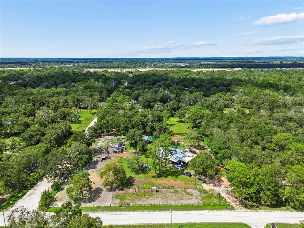 An aerial view shows a rural property with a house, outbuildings, and surrounding wooded land — 18020 RIGSBY ROAD, SPRING HILL, FL