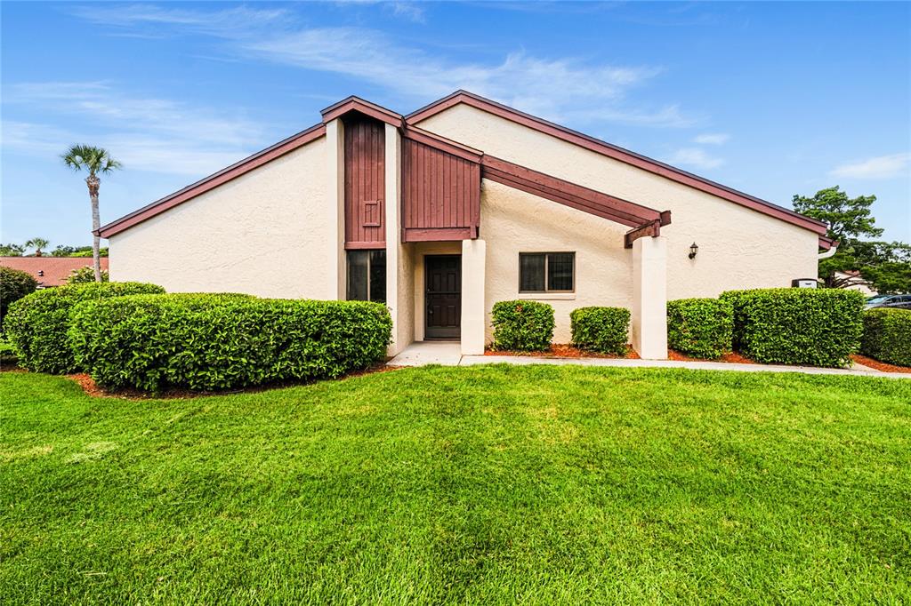 A single-story house with beige stucco walls, brown wood accents, and a manicured front lawn — 101 GRAND PLAZA DRIVE UNIT D60, ORANGE CITY, FL