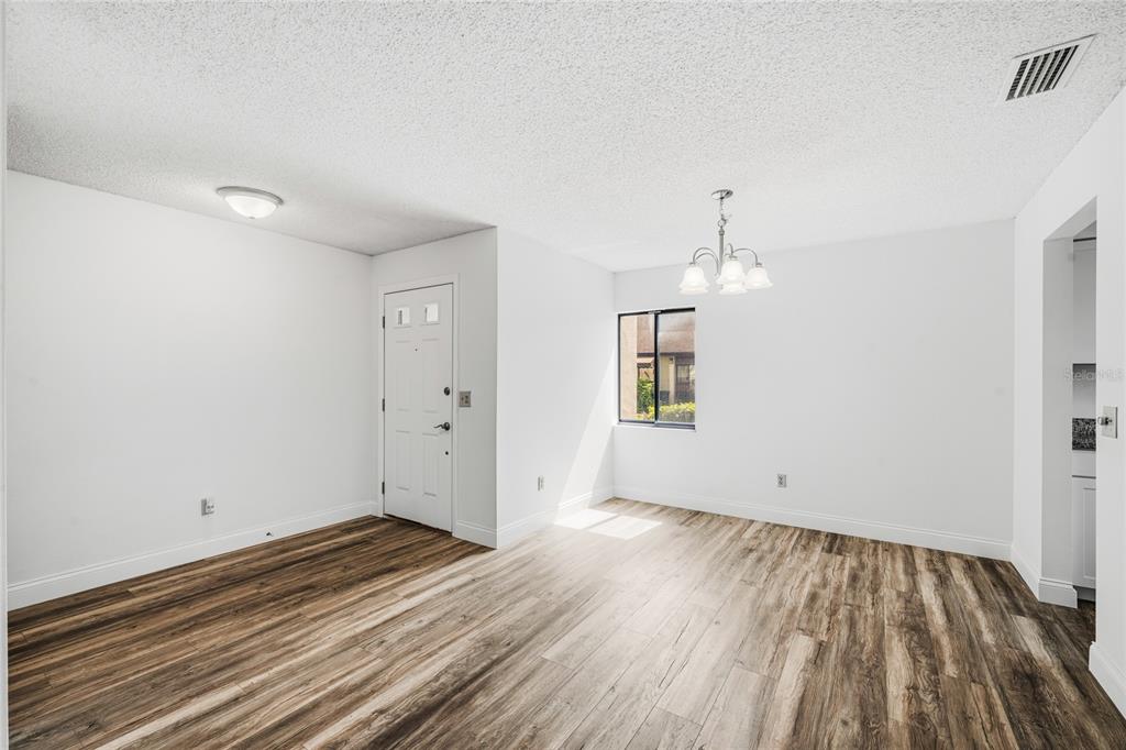 An empty room with white walls, wood-look flooring, a chandelier, and a front door — 101 GRAND PLAZA DRIVE UNIT D60, ORANGE CITY, FL