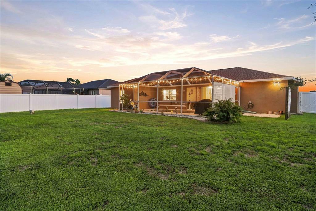 A backyard view of a single-story house with a screened-in patio and white vinyl fencing — 2144 SMYER AVENUE, NORTH PORT, FL