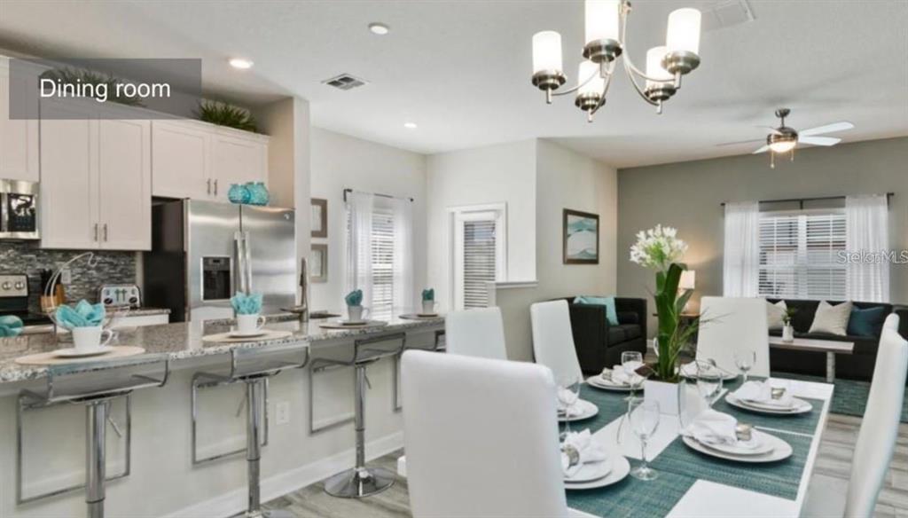 A dining area and kitchen breakfast bar feature white cabinetry, granite countertops, and modern lighting — 1592 SLICE WAY, DAVENPORT, FL