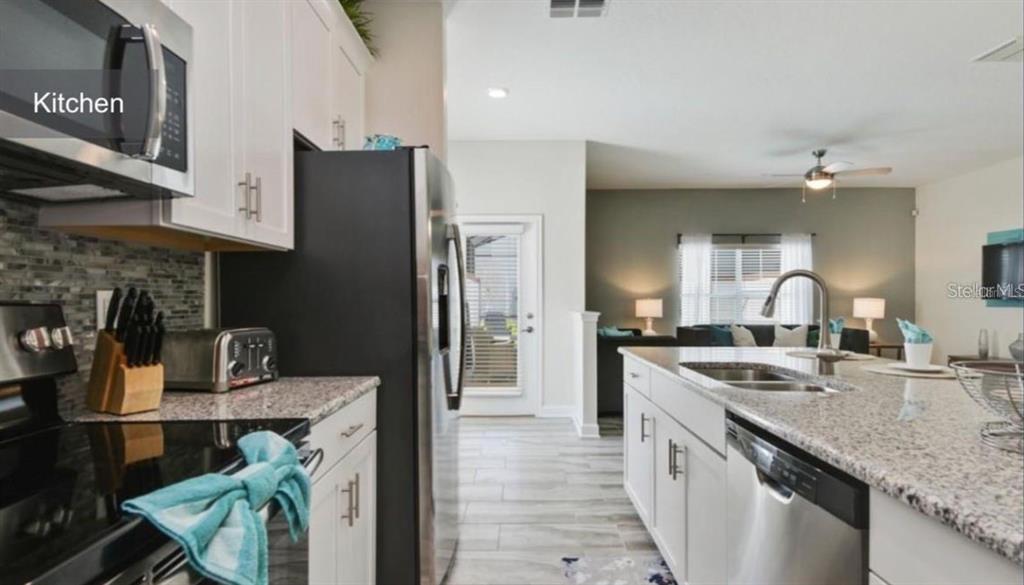 A kitchen with white cabinets, granite countertops, stainless steel appliances, and a central island — 1592 SLICE WAY, DAVENPORT, FL