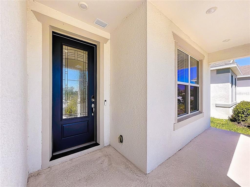 A dark front door with a glass insert sits on a covered porch with stucco walls — 1868 GROVELINE ROAD, ST CLOUD, FL