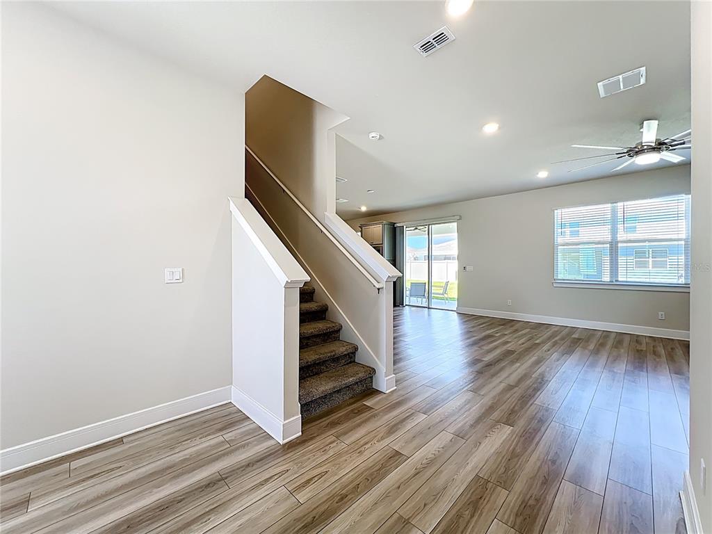 An interior view shows a staircase with carpeted steps next to a living area with wood-look flooring — 1868 GROVELINE ROAD, ST CLOUD, FL