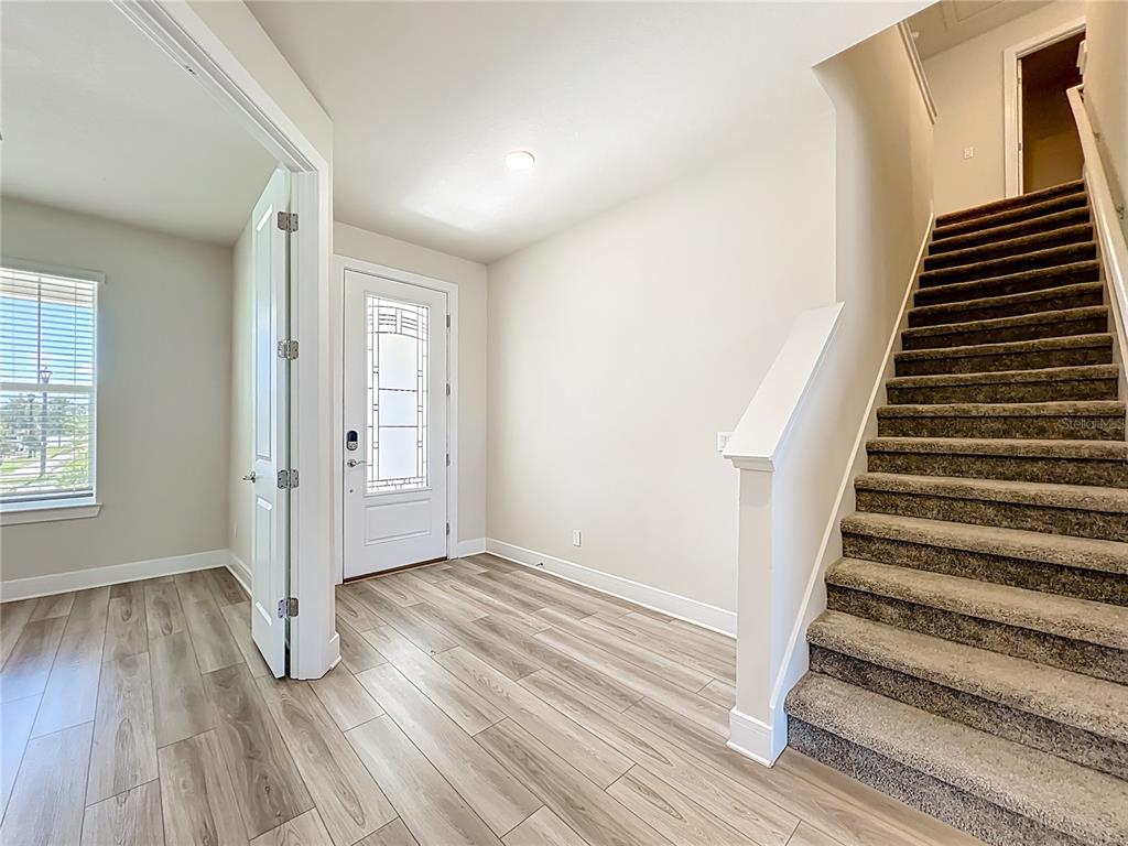 An entryway features light wood-look flooring, a white front door, and carpeted stairs — 1868 GROVELINE ROAD, ST CLOUD, FL
