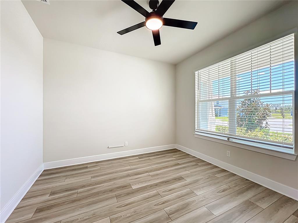An empty room with light-colored walls, wood-look flooring, a ceiling fan, and a large window — 1868 GROVELINE ROAD, ST CLOUD, FL
