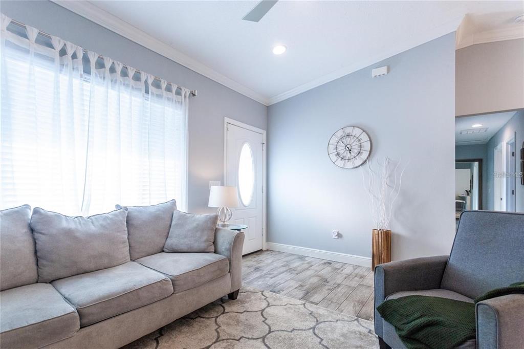 A living room features light blue walls, wood-look tile flooring, a gray sofa, and armchair — 8 SEQUOIA DRIVE COURSE, OCKLAWAHA, FL