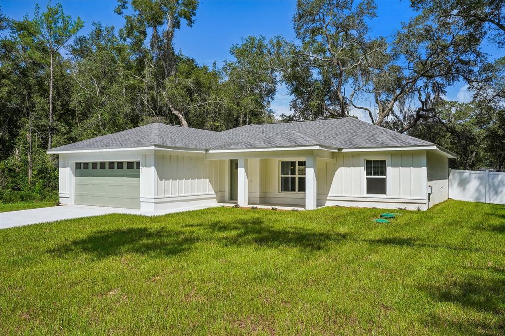 A single-story white house with board-and-batten siding, a gray roof, and a green garage door — 1194 W VIRGINIS DRIVE, CITRUS SPRINGS, FL
