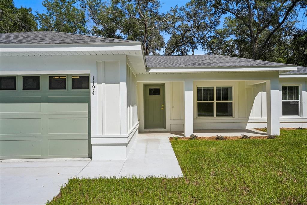 A white house exterior features a sage green garage door, matching front door, and covered porch — 1194 W VIRGINIS DRIVE, CITRUS SPRINGS, FL