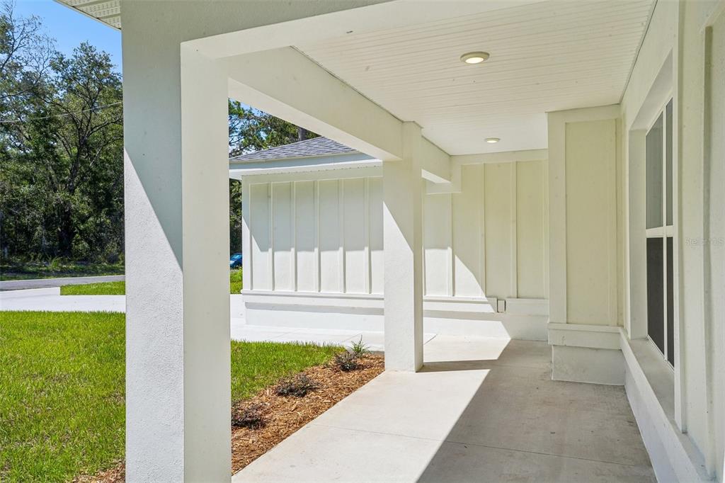 A covered concrete porch with white columns and board-and-batten siding overlooks a grassy yard — 1194 W VIRGINIS DRIVE, CITRUS SPRINGS, FL
