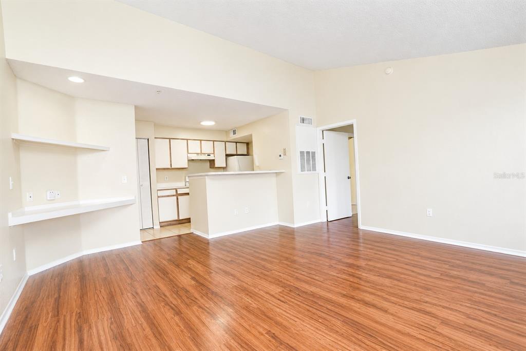 An open-concept living area features wood-look flooring, a breakfast bar, and built-in shelving — 2208 ANTIGUA PLACE UNIT 932, KISSIMMEE, FL
