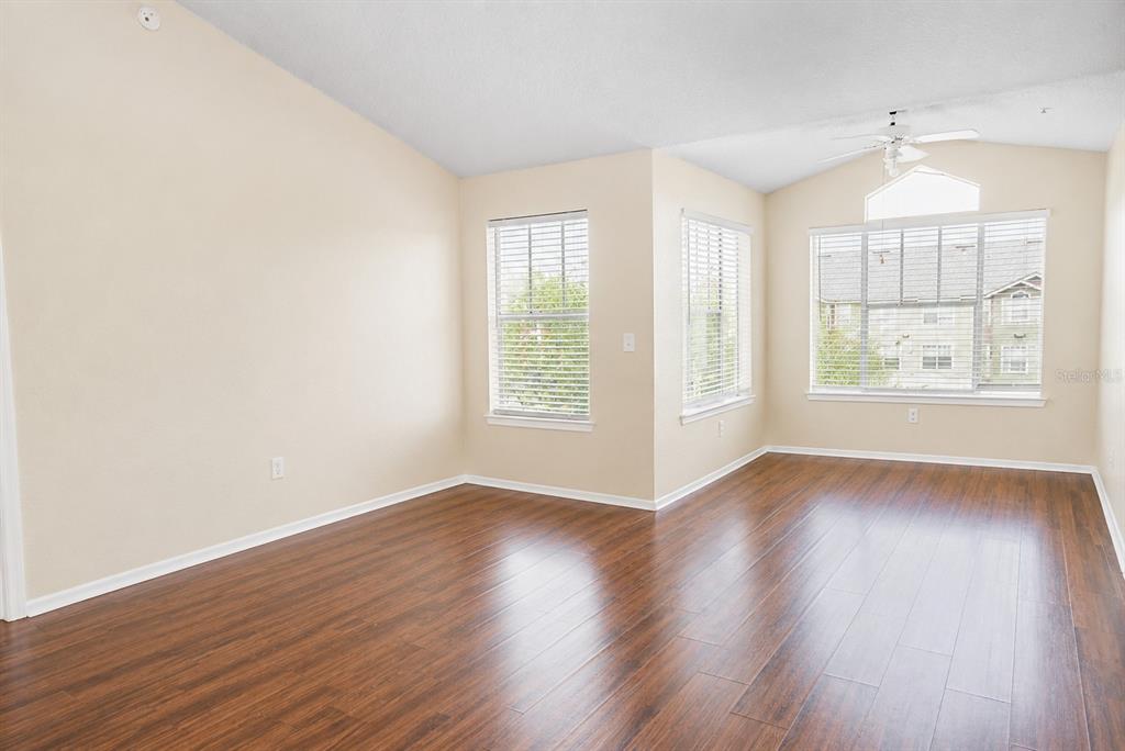 An empty room with vaulted ceilings, wood-look flooring, and several windows with white blinds — 2208 ANTIGUA PLACE UNIT 932, KISSIMMEE, FL