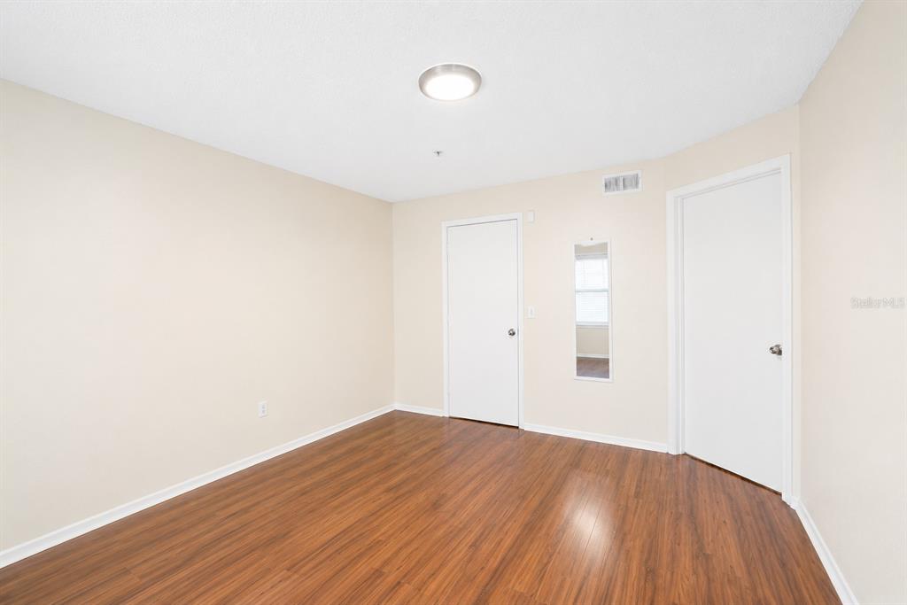 An empty bedroom with beige walls, wood-look flooring, two white doors, and a ceiling light — 2208 ANTIGUA PLACE UNIT 932, KISSIMMEE, FL