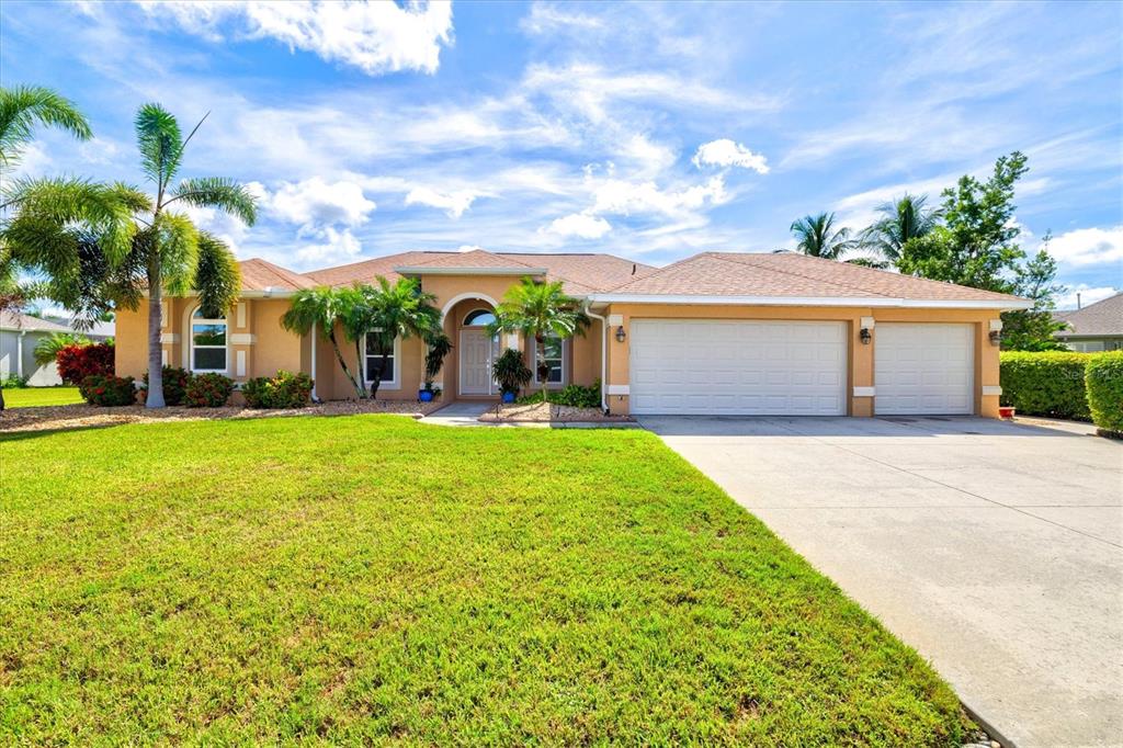 A tan house exterior features a palm tree, rock landscaping, and a two-car garage — 203 LAKE VICTORIA COURT, ENGLEWOOD, FL